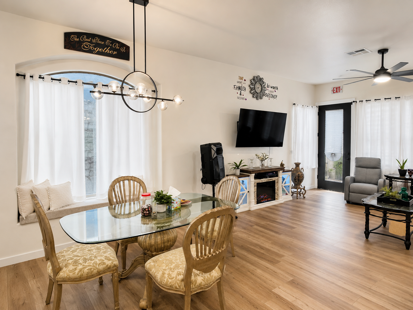 Bright dining and living area with glass table, chandelier, window seat, fireplace, and wall art